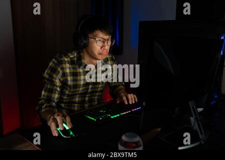 Asiatische Mann Gamer in Kopfhörer mit Hand gestresst fühlen depressiv oder wütend schockiert, wenn das Videospiel auf dem Computer Angst und verärgert für Fehler verlieren, vi Stockfoto