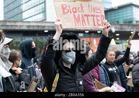 Schwarze Leben Materie Protest Manchester UK. Frau mit Maske hält Schild vor Piccadilly Busbahnhof Gebäude mit Menge im Hintergrund Stockfoto