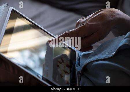 Frau arbeitet von zu Hause aus und scrollt mit ihrem Zeigefinger auf einem Tablet-Computer oder Mobilgerät durch eine Seite Stockfoto