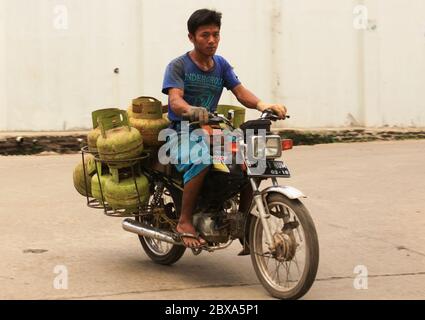 JAKARTA, INDONESIEN - 30. Mai 2013: Indonesischer Lieferarbeiter auf Motorrad mit Butangastanks gestapelt Stockfoto