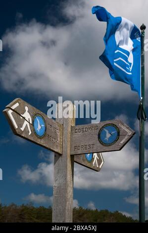 Flagge und zweisprachiger Holzfußweg, Schild zum Strand und Wald in der Nähe des Parkplatzes am Newborough Beach auf der Isle of Anglesey. Stockfoto