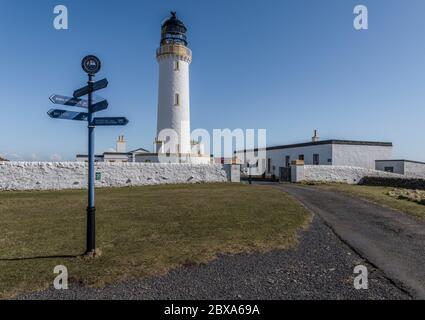 Wegweiser zu verschiedenen Zielen an der Mull of Galloway mit dem Leuchtturm im Hintergrund, der sich am südlichsten Punkt Schottlands befindet. Stockfoto