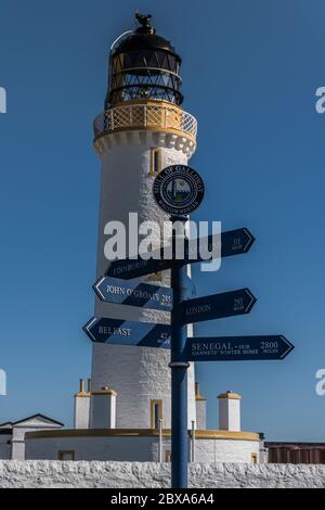 Wegweiser zu verschiedenen Zielen an der Mull of Galloway mit dem Leuchtturm im Hintergrund, der sich am südlichsten Punkt Schottlands befindet. Stockfoto