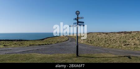 Panorama der Wegweiser zu verschiedenen Zielen am Mull of Galloway, dem südlichsten Punkt Schottlands mit einem breiten Meereshorizont im Hintergrund Stockfoto