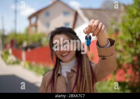 Nettes lächelndes Mädchen mit langen Dreadlocks und Brillen zeigt Bündel von Hausschlüssel in einer Hand in Richtung der Kamera. Immobilienmakler Konzept Stockfoto