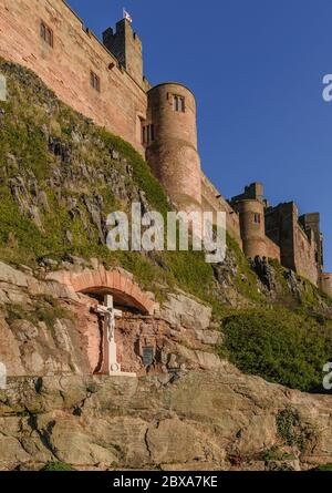 Das Kriegsdenkmal von Bamburgh, das in der Klippe unterhalb der Mauern von Bamburgh Castle in Northumberland, England, unter einem sonnendurchfluteten, klaren blauen Himmel errichtet wurde. Stockfoto