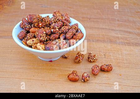 Plateful von Bio-Sauce bedeckt Erdnüsse und verschüttete Sauce bedeckt Erdnüsse auf Holzhintergrund Stockfoto