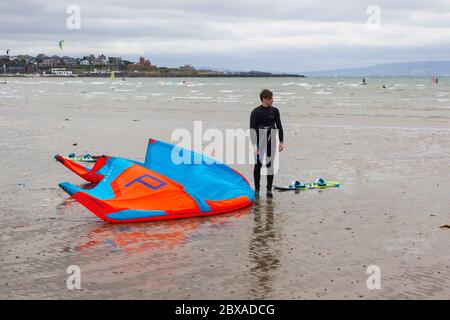 6. Juni 2020 ein trüber Tag und ein junger Kitesurfer macht sich neben seinem Equipment am Ufer des Ballyholme Beach in Bangor, Nord, eine willkommene Pause Stockfoto