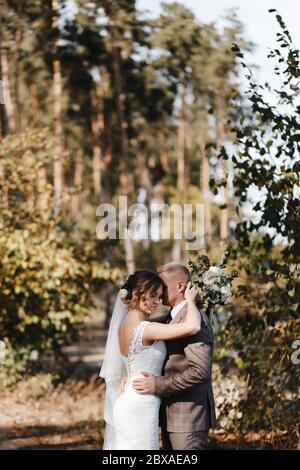 Braut und Bräutigam umarmen sich im Hintergrund der Bäume im Wald. Porträt von Braut und Bräutigam Stockfoto