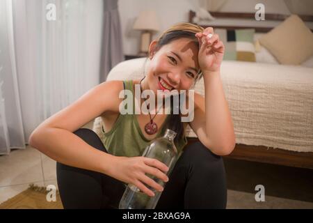 Asiatische Mädchen tun Fitness zu Hause - junge schöne und glückliche chinesische Frau Trinkwasser Flasche fröhlich nach Sport Training lächelnd positiv auf sie Stockfoto