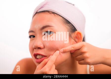 Junge schöne wütend und verärgert asiatische chinesische Frau mit Akne Pooping Kopf der Pickel mit ihren Fingern auf dem Spiegel Reinigung der Haut in Beauty Treat Stockfoto