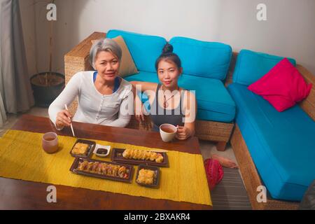 Asiatische fröhliche weibliche Freunde mit japanischen Sushi zum Mittagessen - glücklich und attraktiv Frau und ihre Freundin essen Sushi-Rollen zu Hause genießen tog Stockfoto