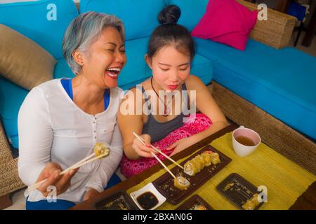 Asiatische fröhliche weibliche Freunde mit japanischen Sushi zum Mittagessen - glücklich und attraktiv Frau und ihre Freundin essen Sushi-Rollen zu Hause genießen tog Stockfoto