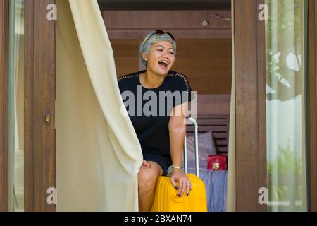Lifestyle-Porträt von natürlichen attraktiv und glücklich mittleren Alters asiatische Frau in stilvollen Sommerkleid Ankunft im Hotel Zimmer öffnen Balkon Tür suchen Stockfoto
