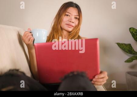 Junge attraktive und schöne asiatische indonesische Frau in Jeans und Casual Top zu Hause arbeiten entspannt und glücklich mit Laptop-Computer-Networking mit Stockfoto