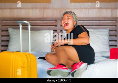 Reise Glückseligkeit. Natürliche Lifestyle-Porträt von glücklichen und attraktiven 40er bis 50er Jahre reifen asiatischen Frau mit grauen Haaren Ankunft im Hotelzimmer aufgeregt auf Bett j Stockfoto