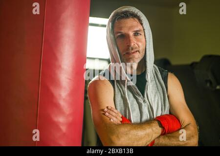 Sport Fitness Lifestyle Porträt von jungen glücklich und verschwitzt Mann Boxen im Fitnessstudio Training schwitzt in Hoodie Weste Training auf schwere Tasche suchen cool in e Stockfoto