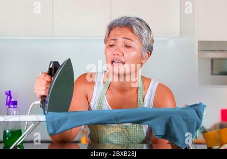 Verzweifelt und gestresst mittleren Alters asiatische Frau Bügeln in Stress zu Hause Küche Gefühl überwältigt und müde von der Arbeit Hausarbeiten in hilflos Stockfoto