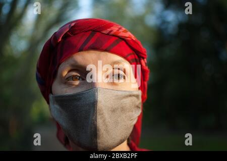 Reife Frau trägt handgefertigte textile Gesichtsmaske als Accessoire und Schutzelement während des sonnigen Frühlings im Park wegen Coronavirus Stockfoto
