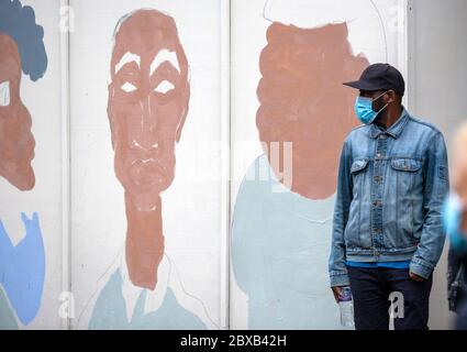 Mann, der eine Gesichtsmaske, eine Baseballmütze und eine Jeansjacke trägt, steht vor einem bemalten Wandgemälde, beim BLM UK Protest, Whitehall, London UK Stockfoto