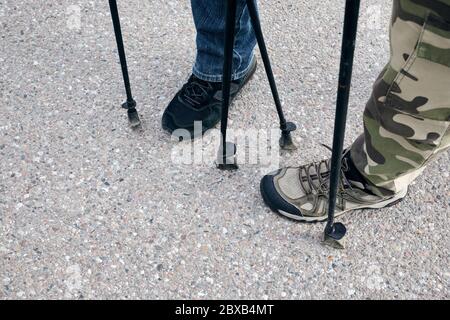 Nordic Walking Konzept im Freien. Männer Füße Beine in Trekkingschuhen stehen auf dem Asphaltweg. Draufsicht. Stockfoto