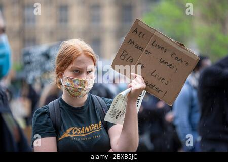 Junge Frau, die eine Gesichtsmaske und ein Los Angeles T-Shirt trägt, hält ein selbstgebautes Schild hoch, beim Protest der Black Lives Matter UK, Parliament Square, London UK Stockfoto