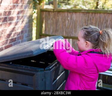 Corona Kompostierung, 4 Jahre altes Mädchen vor der Schule Entleeren der Komposteimer, immer Ihr Kind interessant im Garten. Corona Lockdown Gartenarbeit Stockfoto