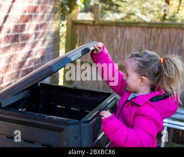 Corona Kompostierung, 4 Jahre altes Mädchen vor der Schule Entleeren der Komposteimer, immer Ihr Kind interessant im Garten. Corona Lockdown Gartenarbeit Stockfoto