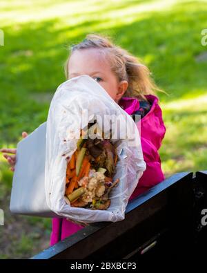 4-jähriges Mädchen, das den Kompostbehälter entleert, Ihr Kind in der Gartenarbeit interessant macht, Vorschulkinder lernen, den Kompostbehälter zu leeren Stockfoto