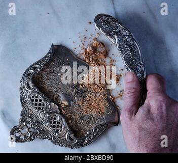 Ein verzierten Metall Whiskesen und Pfanne für die Reinigung der Tabelle von Krümeln zwischen Gängen. Eine männliche Hand fegt die Krümel in die Pfanne. Stockfoto