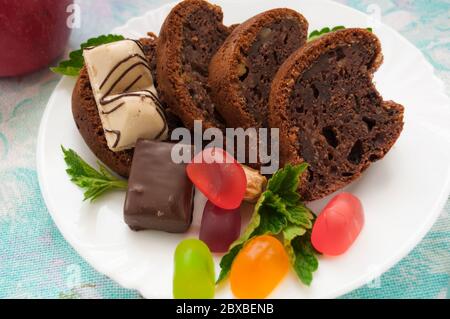 Stücke von Schokoladenkuchen und bunte Gelee Süßigkeiten auf einem weißen Teller mit Minze verziert Nahaufnahme auf einem Hintergrund von farbigen Serviette Stockfoto