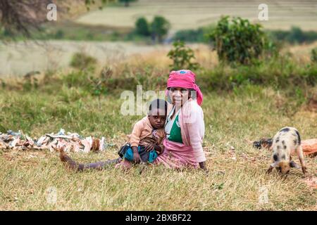 Müde afrikanische Frau mit Kind auf dem grünen Feld sitzen. Zentralmadagagagaga Stockfoto