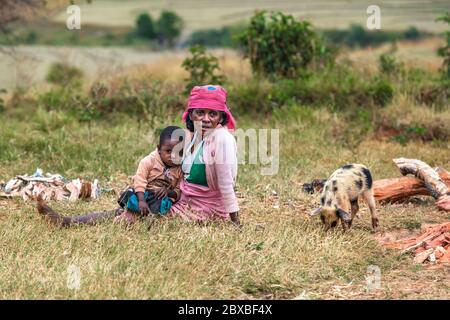 Müde afrikanische Frau mit Kind auf dem grünen Feld sitzen. Zentralmadagagagaga Stockfoto