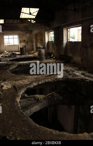 Große Löcher im Holzboden des obersten Stockwerks einer verlassenen Fabrik mit rostigen Trommeln, Schmutz und Trümmern. Stockfoto