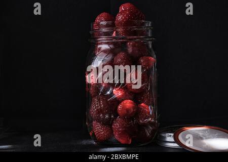 Bio-Erdbeeren in einem Mason Ball Jar in der Morgensonne auf schwarzem Hintergrund rechts im Bild Stockfoto