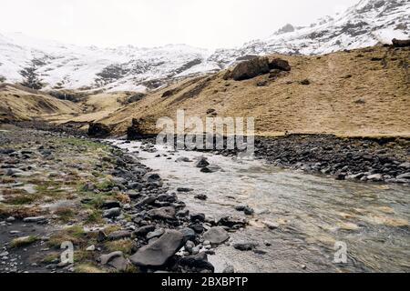 Seichter kleiner Gebirgsfluss, fließt von schneebedeckten Bergen in die Schlucht, auf einer Kaskade von Wasserfällen. Schneebedeckter Berggipfel und Fuß hinein Stockfoto