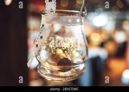 Hängende runde Glasbehälter als Vase mit weißem Band mit Herzen verziert verwendet. Abstrakter verschwommener Hintergrund. Stockfoto