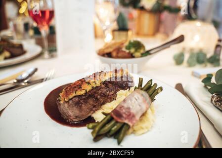 Mahlzeit auf festlichem Tisch serviert. Stück Rindfleisch mit Kartoffelpüree und grünen Bohnen auf weißem Teller. Feier, Party, Geburtstag oder Hochzeit Stockfoto