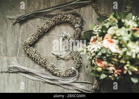 Hochzeitsdekoration von oben. Trauringe an Blumenherz und Brautstrauß auf grauem Steinhintergrund gebunden. Konzept für Hochzeitstag. Stockfoto