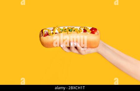 Cropped Ansicht von jungen Mädchen mit leckeren Hot Dog mit Senf und Ketchup auf orangefarbenem Hintergrund Stockfoto