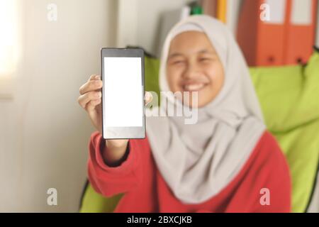Glücklich fröhlich asiatisch muslimisch Mädchen trägt Hijab zeigt ihr Smartphone, Telefon Vorlage Mock up, selektive Fokus auf Telefon Stockfoto