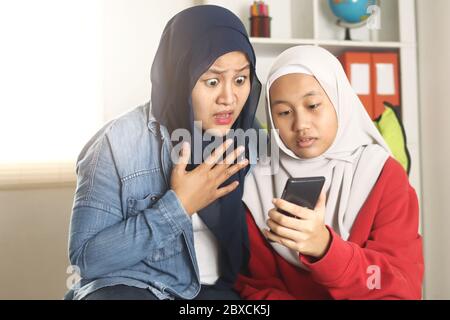 Asiatische muslimische Mutter und Tochter schockiert und besorgt, wenn sie auf ihr Telefon, Surfen im Internet und finden schlechte Nachrichten in sozialen Medien, Casual Lifestyle Stockfoto