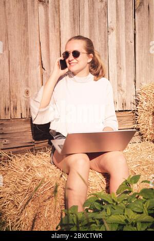Junge Frau, die auf einem Laptop draußen auf einem Bauernhof arbeitet Stockfoto