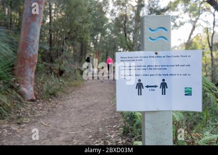 Ein Schild auf einer Buschwanderbahn im nördlichen Vorort Sydney, Australien, warnt Wanderer davor, 1.5 Meter voneinander entfernt zu bleiben, mit verschwommenen Menschen im Hintergrund Stockfoto