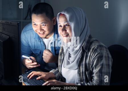Ein Paar las einen Vertrag, der nachts per E-Mail empfangen wurde, überprüfte die Details und stellte eine Verbindung mit dem Computer online, eine glückliche lächelnde Geste Stockfoto