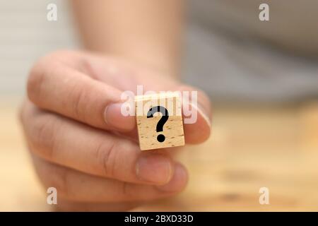 Ein Mann hält und zeigt Holzblock mit Fragezeichen darauf, Konzept der Frage oder Zweifel, selektive Fokussierung mit verschwommenem Hintergrund Stockfoto