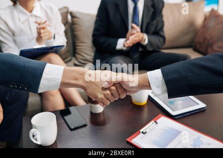 Geschäftsleute, die nach Abschluss des Geschäfts mit Finanzdokumenten die Hände über den Tisch legen Stockfoto