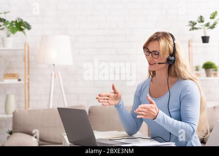 Geschäftstreffen von zu Hause aus. Frau in Brille und Kopfhörer, die auf dem Laptop spricht Stockfoto