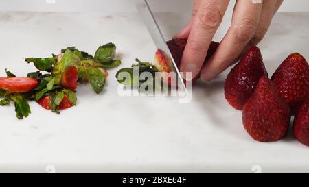 Frau schneidet frische reife Erdbeeren zum Dessert, Nahaufnahme auf weißem Hintergrund Stockfoto