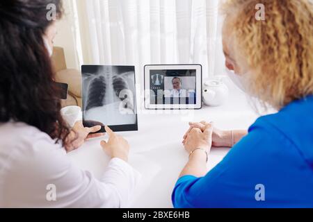 Leitender Patient, der einen Arzt aufruft, der die Röntgenaufnahme des Brustkorbs mit einem erfahrenen Pulmologen per Videoanruf bespricht Stockfoto